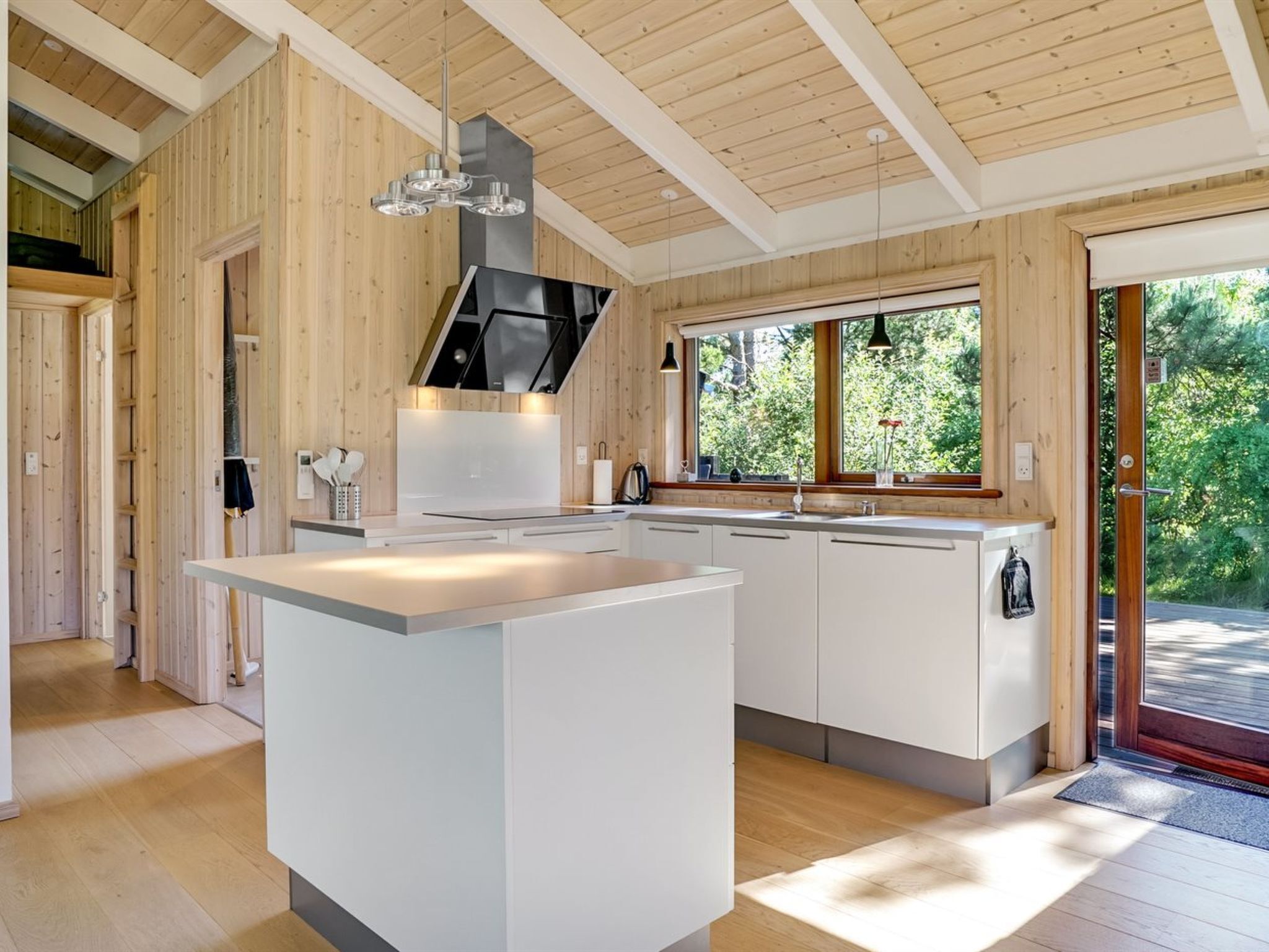 Une cuisine moderne dotée d’un îlot central, de murs en bois et d’une grande fenêtre offrant une vue sur la verdure.