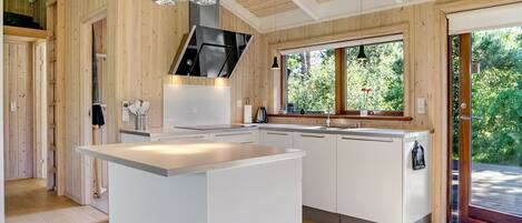 Une cuisine moderne dotée d’un îlot central, de murs en bois et d’une grande fenêtre offrant une vue sur la verdure.
