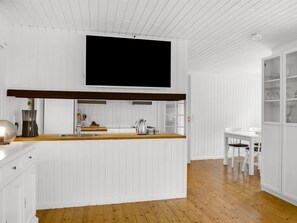 A modern kitchen with a flat-screen TV mounted above the counter, wooden flooring, and white cabinetry.