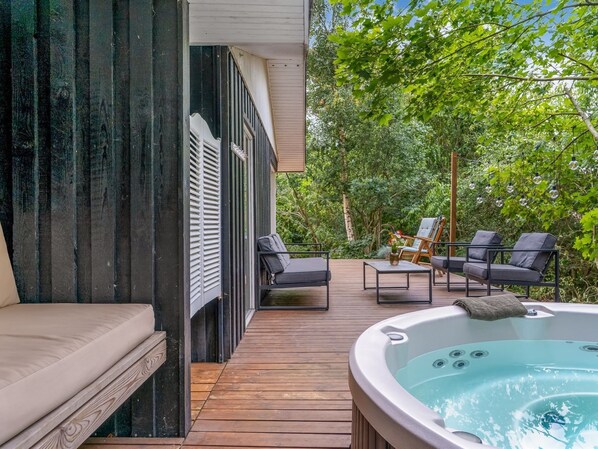 A wooden deck with a hot tub, lounge chairs, and a sofa.