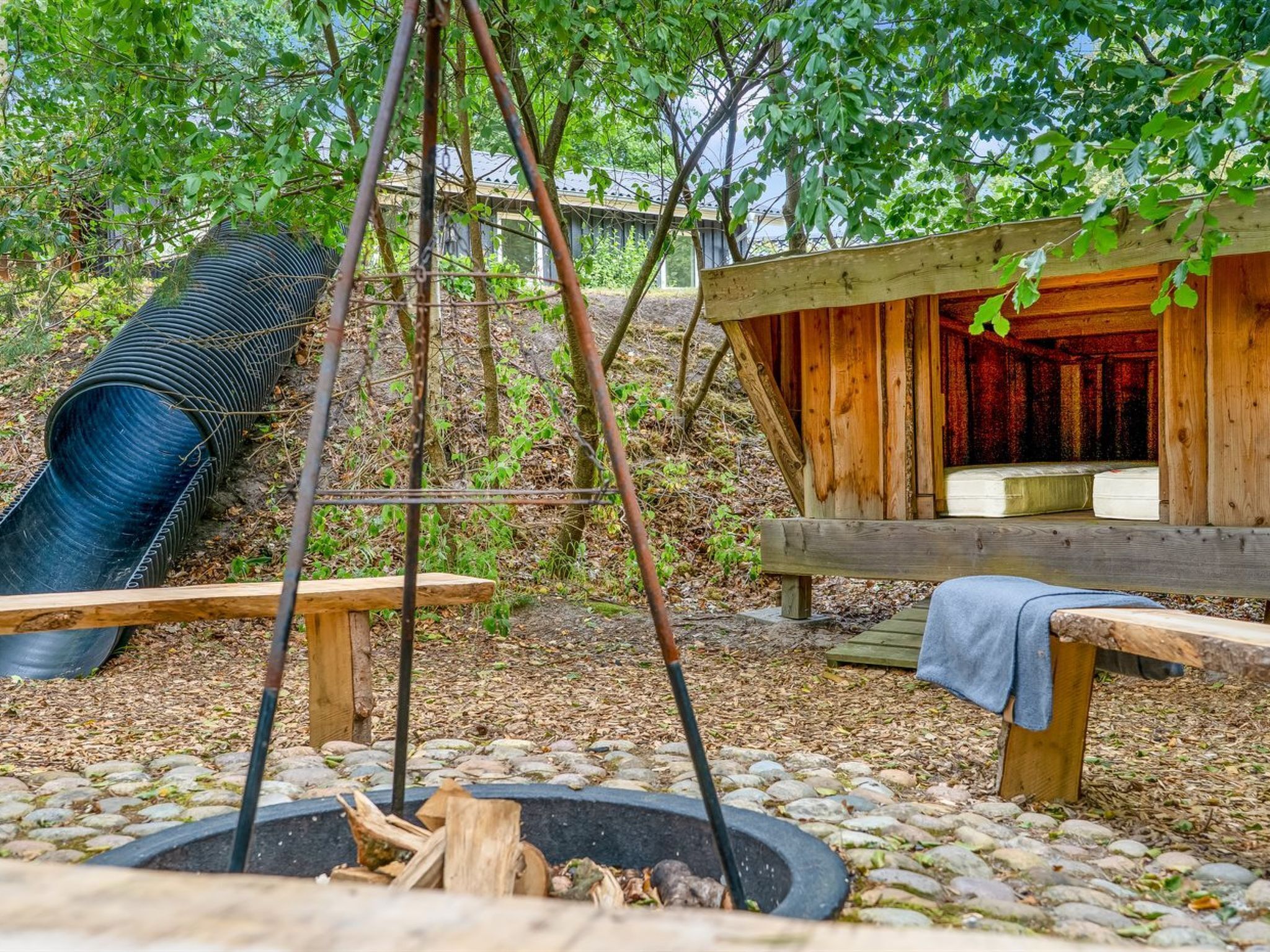 Une structure en bois installée à l’extérieur, comprenant un foyer, un toboggan et un banc.