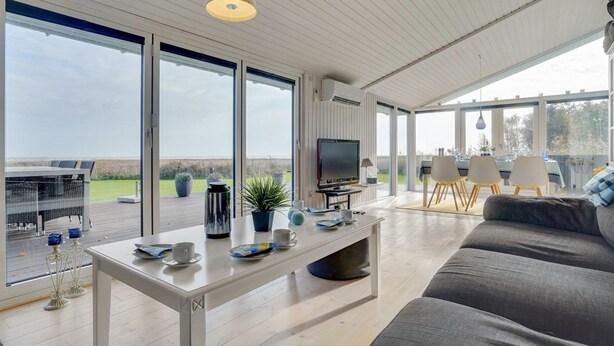 Un vaste espace de vie comprenant un grand canapé, une table à manger et un téléviseur. De grandes fenêtres offrent une vue sur l’extérieur.