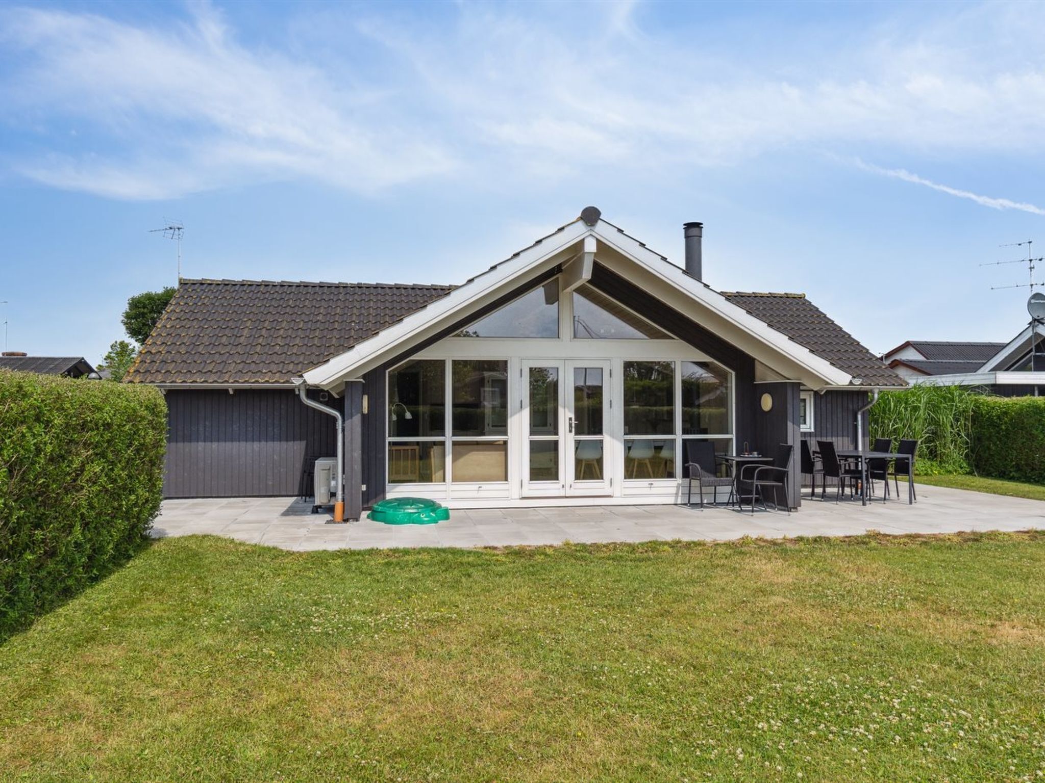 Een modern huis met een grote glazen voordeur, een overdekt terras met tuinmeubilair en een verzorgd gazon.