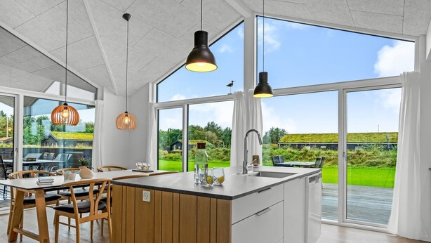 Eine moderne Küche mit einer großen Kochinsel, Holzkreisen, Pendelleuchten und großen Fenstern mit Blick ins Freie.