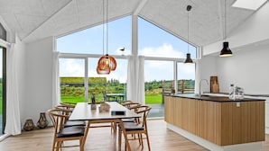 Ein geräumiger Essbereich mit großem Tisch und Stühlen, eine Küche mit Holdekor-Schränken und große Fenster mit Blick ins Freie.