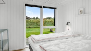 Ein Schlafzimmer mit großem Fenster, einem Bett, einem Nachttisch und einer Pendelleuchte.