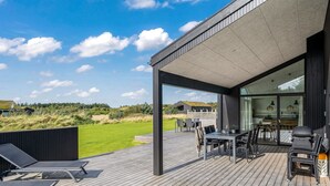 Eine moderne Außenterrasse mit Essbereich, Liegestühlen und Blick auf die Landschaft.