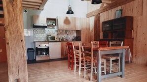 A kitchen with wooden cabinets, a dining table with chairs, a microwave, and a hanging light fixture.