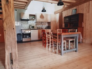 A kitchen with wooden cabinets, a dining table with chairs, a microwave, and a hanging light fixture.