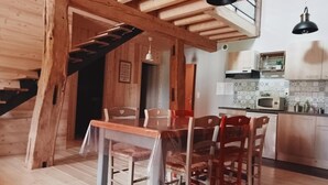 A wooden interior with a dining table and chairs, a kitchen area with appliances, and a staircase.
