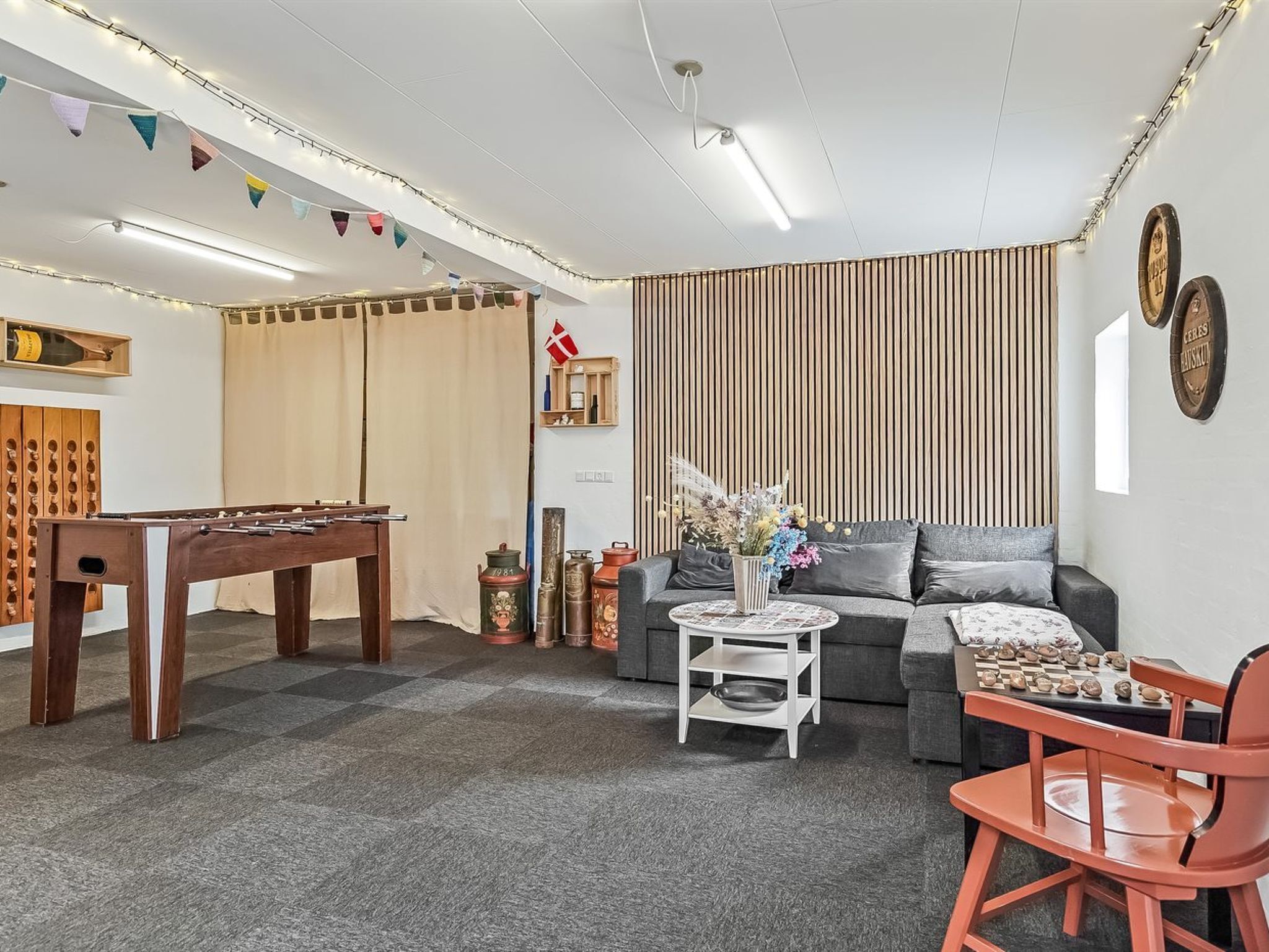 Een gezellige woonkamer met een tafelvoetbaltafel, een bank, een salontafel en een rode fauteuil.