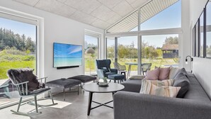 Ein modernes Wohnzimmer mit großem Fenster, Flachbildfernseher und gemütlicher Sitzecke.