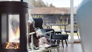 Ein modernes Wohnzimmer mit Kamin, gemütlicher Sitzgelegenheit und einem großen Glasfenster zum Außenbereich.