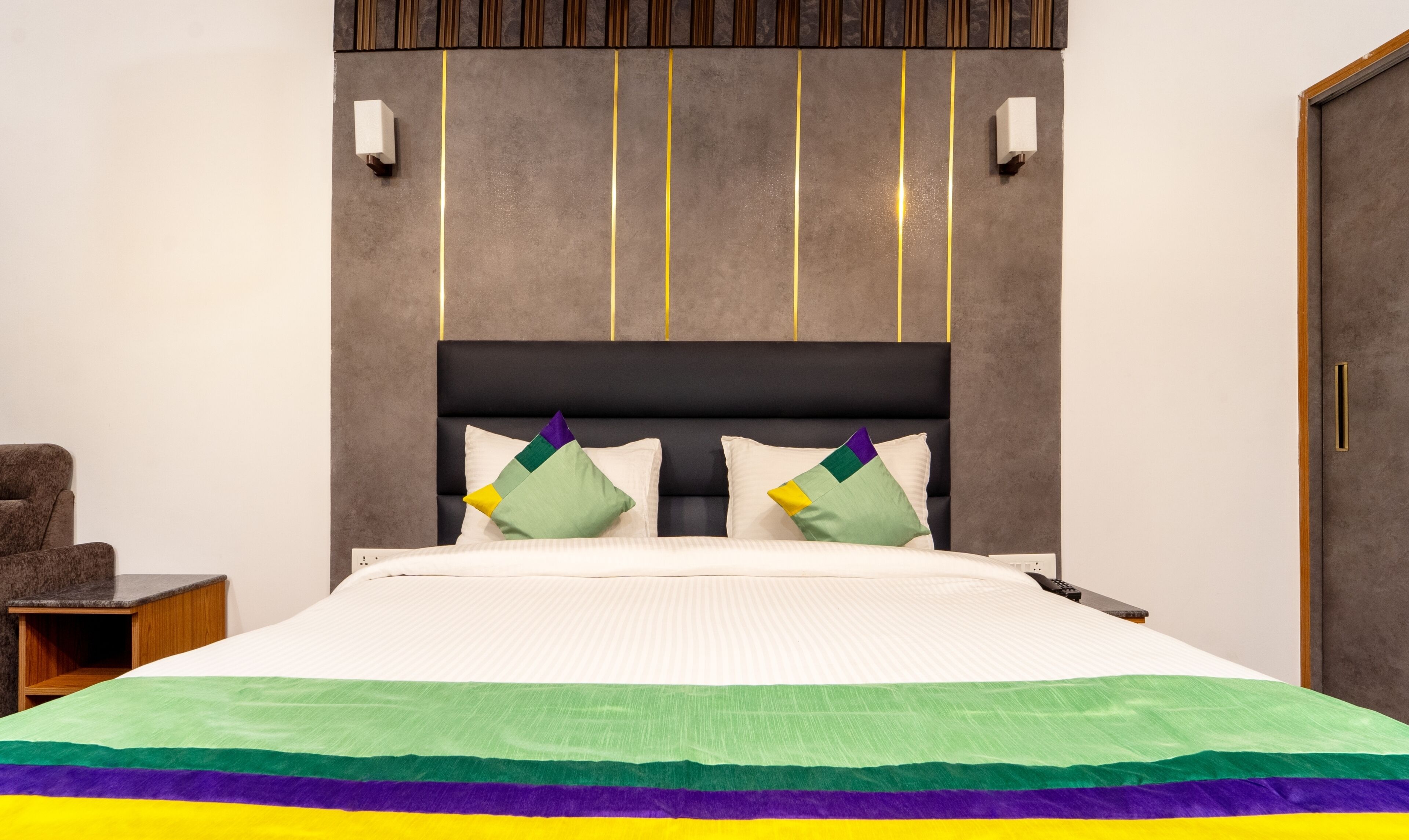 A modern bedroom with a large bed, two bedside lamps, a nightstand, and a wooden chair.
