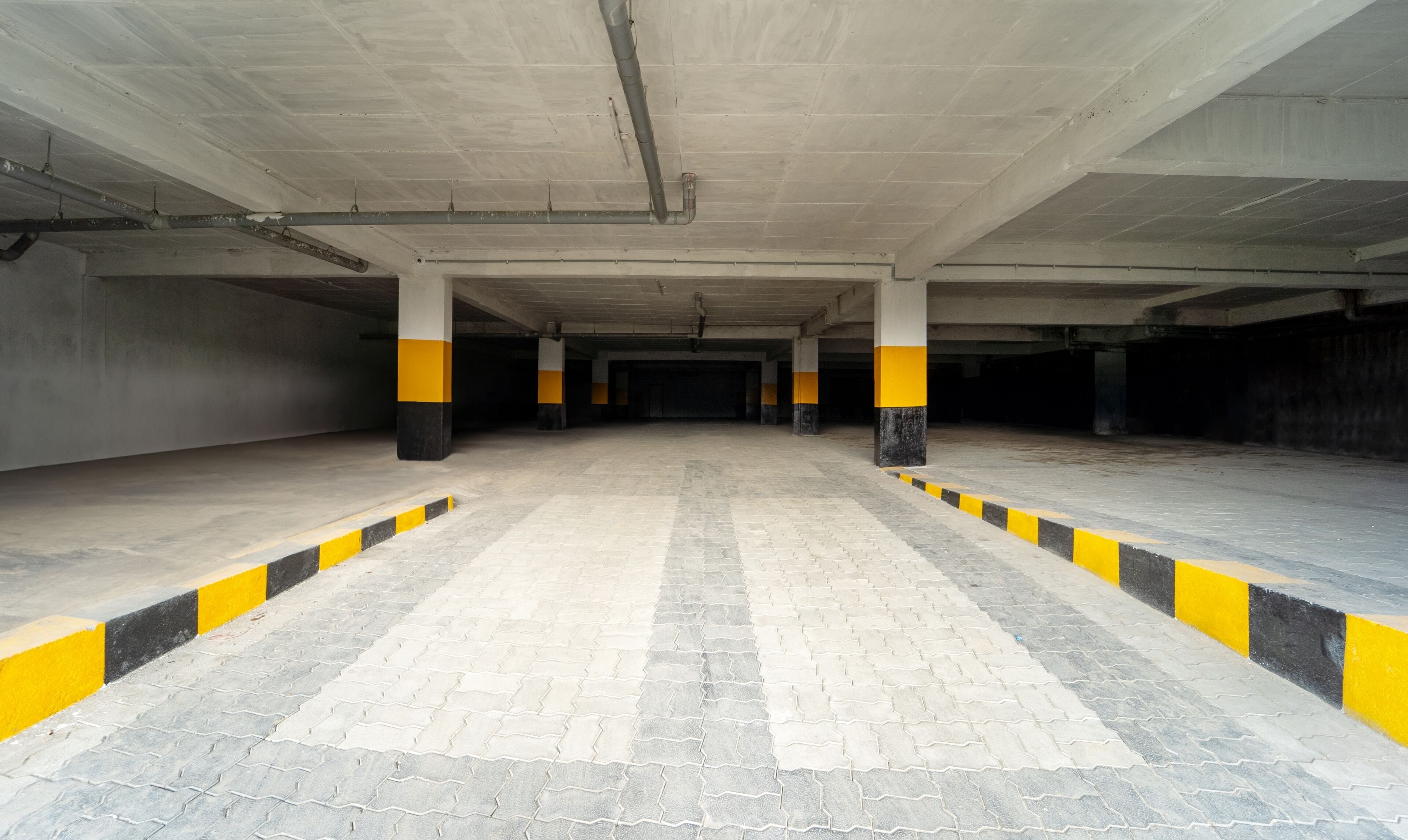 Un estacionamiento vacío con pilares de hormigón y barreras a rayas negras y amarillas.