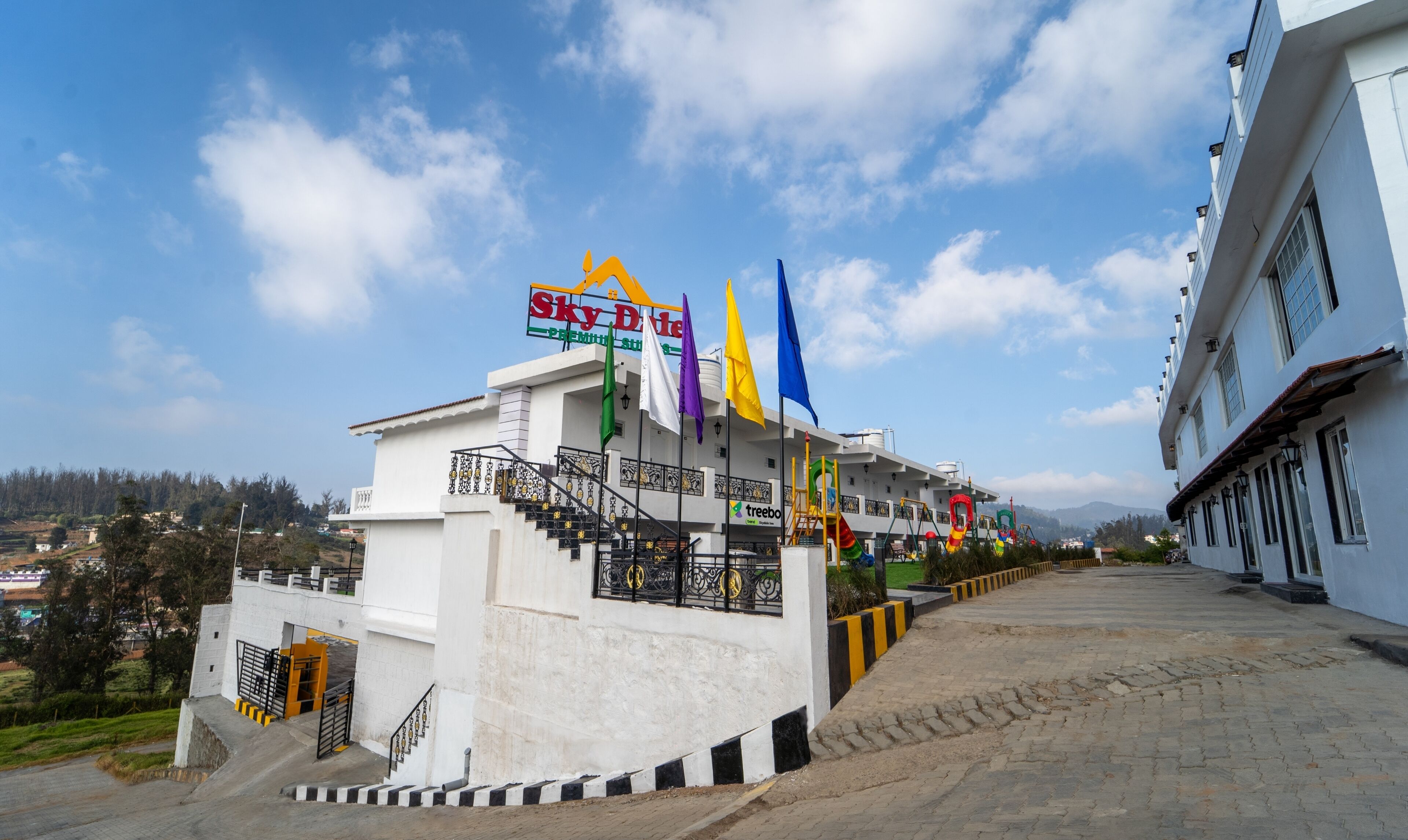 A hotel with a staircase leading to the entrance, multiple flags, and a clear sky.
