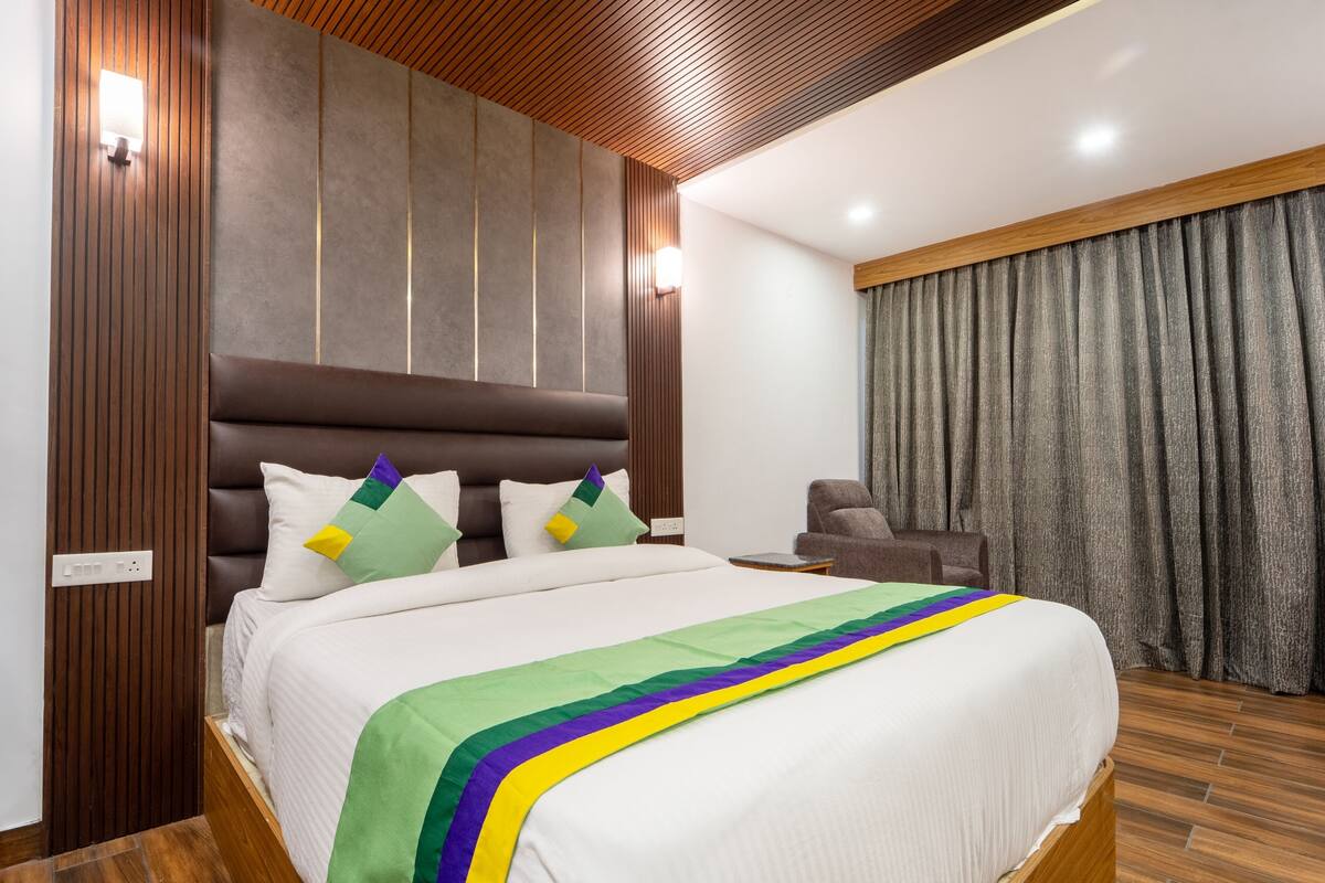 A modern hotel room with a large bed, wooden paneling, and a view of the city.