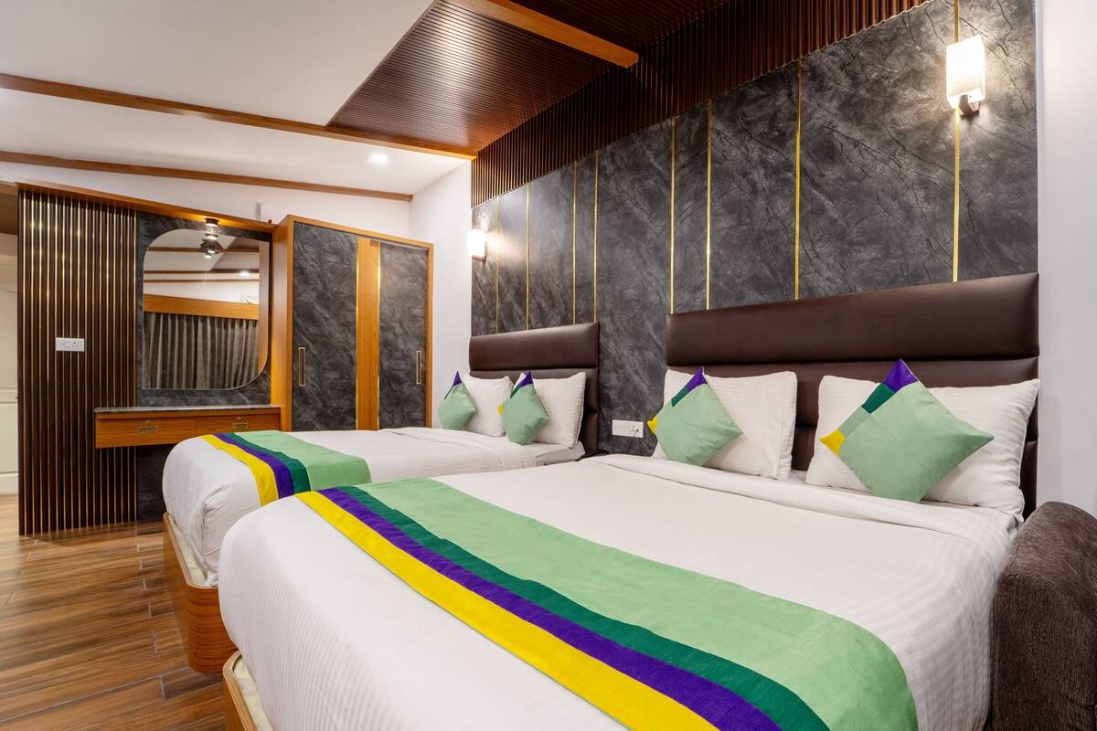 A hotel room with two beds, a wooden wardrobe, and a marble wall with lighting fixtures.