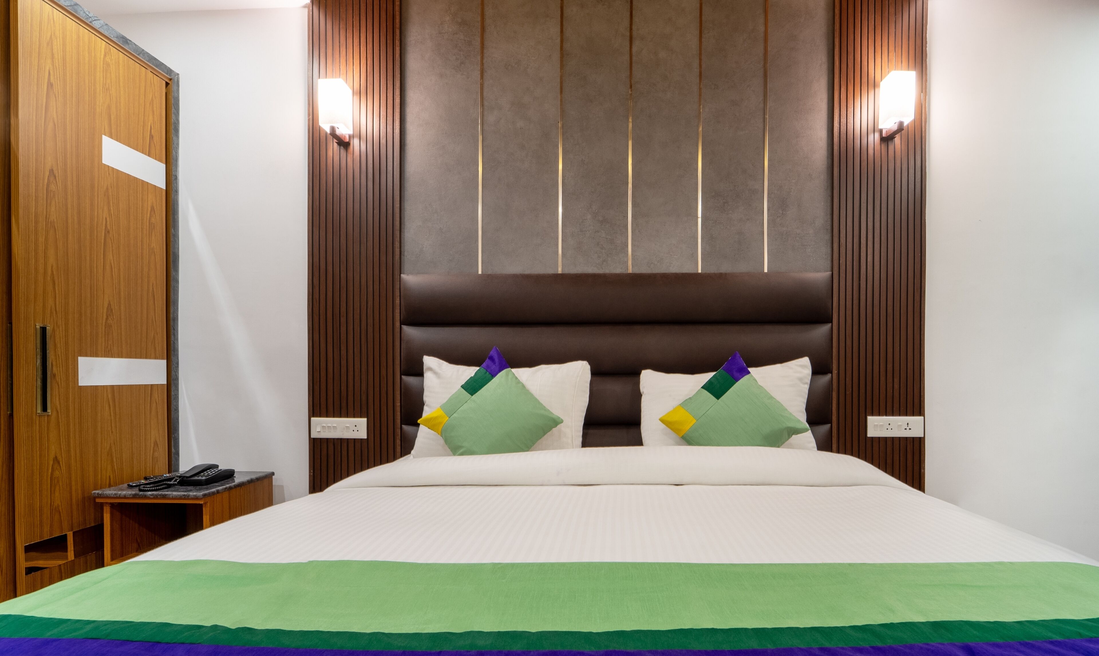 A hotel room with a large bed, wooden wardrobe, and a bedside table with a phone.