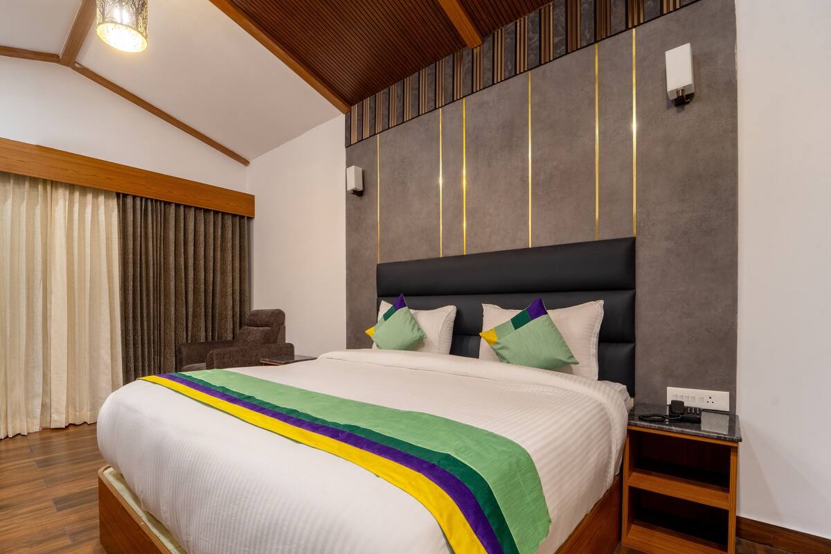 A modern hotel room with a large bed, a wooden headboard, and a nightstand with a phone and remote.