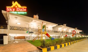 Un hotel llamado Sky Dale con un letrero que indica suites premium. Cuenta con un parque infantil con toboganes y una banca.