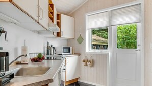 A modern kitchen with white cabinets, a stainless steel sink, a microwave, and a window with a view of greenery. - "Barnet" - 2.2km from the sea by Interhome (Blokhus)
