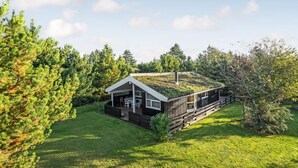 A cabin with a sloped roof, a deck, and a grassy yard surrounded by trees. - "Barnet" - 2.2km from the sea by Interhome (Blokhus)