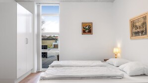 Un dormitorio con dos camas, una ventana que da a una casa, un cuadro en la pared y una lámpara en la mesita de noche.