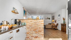 Una cocina moderna con armarios blancos, una pared de ladrillo decorativa y un comedor con sofá y sillas.
