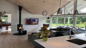 A modern living room with a fireplace, a sofa, a dining area, and large windows offering a view of the outdoors.