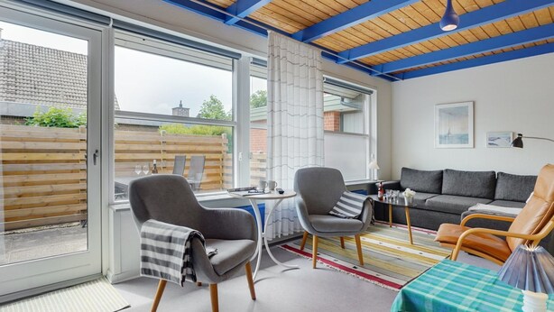 Een moderne woonkamer met een houten plafond, grote ramen en een bank.