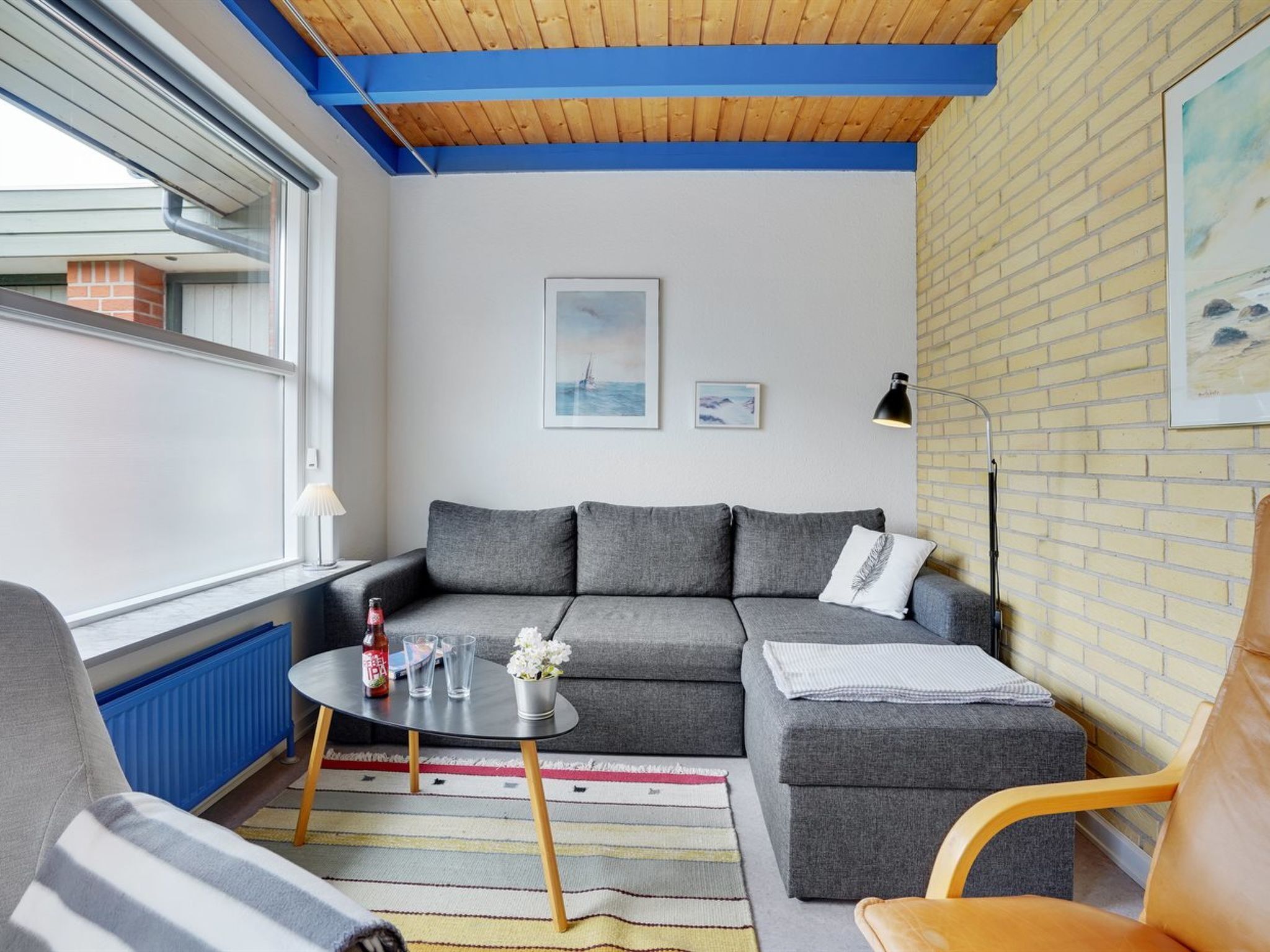 Een moderne woonkamer met een grijze bank, een klein rond tafeltje en een gestreept vloerkleed.