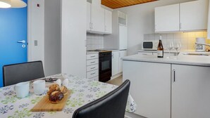 Een moderne keuken met witte kasten, een houten plafond en een blauwe deur.