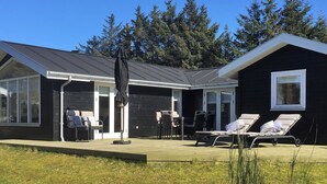 Ein modernes Haus mit überdachter Terrasse, Sitzgelegenheiten im Freien und einem großen Fenster.