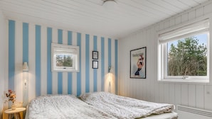 Ein Schlafzimmer mit einem Bett, einem Fenster, einem Wandbild und einem kleinen Tisch mit einer Lampe.