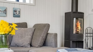 Ein modernes Wohnzimmer mit einer Couch, einem Tisch mit Blumen in einer Vase und einem schwarzen Kaminofen.