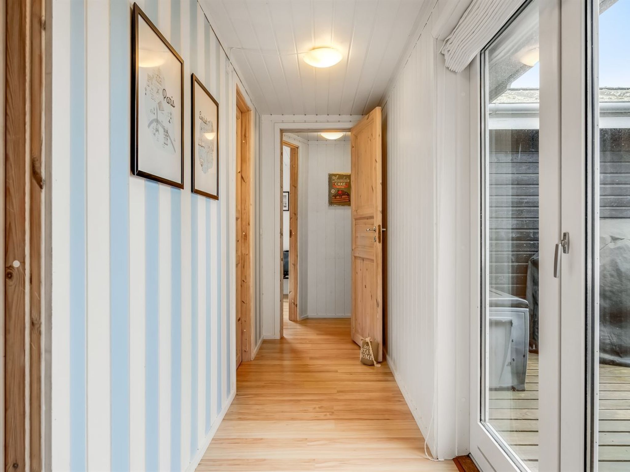 A hallway with striped walls, wooden doors, and a view through a glass door to an outdoor area.