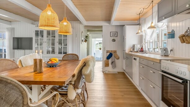 Una cocina amplia con piso de madera, muebles de cocina blancos e iluminación colgante de mimbre.