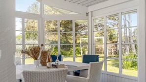 Un patio cubierto con mesa y sillas, ventanas amplias y vistas a la vegetación.