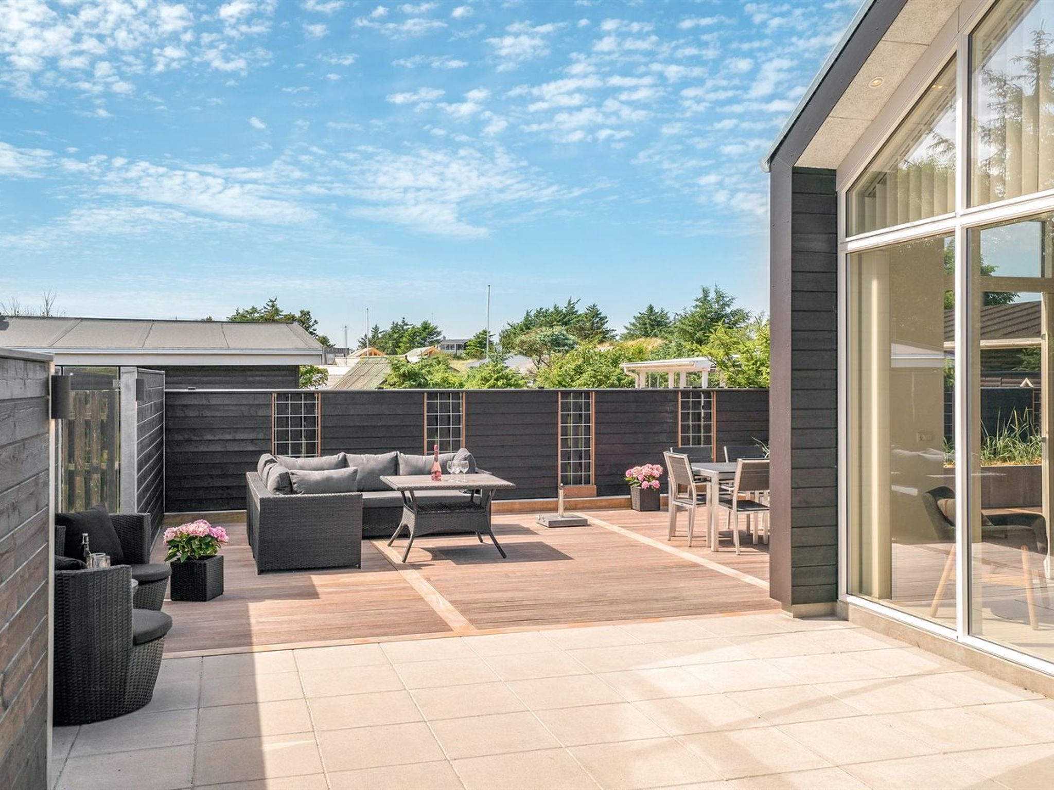 A modern outdoor patio with a wooden deck, grey outdoor furniture, and a glass enclosure.