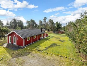 A red building with a sloped roof, a small porch, and a yard with grass and trees.