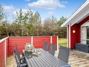 A wooden deck with a table and chairs, a red fence, and a building with a white roof.