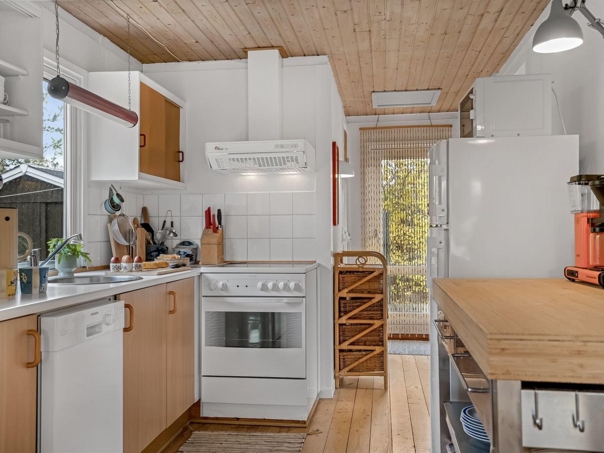 Eine moderne Küche mit weißen Schränken, einem Herd und einer Spüle. Das Zimmer hat eine Holzbalkendecke und ein Fenster mit Blick auf Bäume.