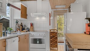 Una cocina moderna con armarios blancos, una estufa y un lavabo. El techo es de madera y hay una ventana con vistas a árboles.
