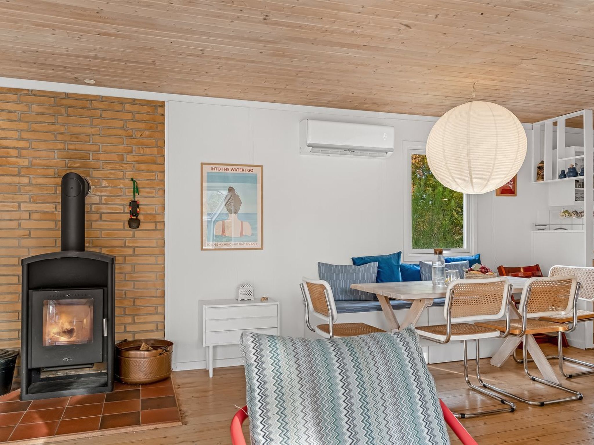 Ein gemütliches Wohnzimmer mit Kamin, eine Essecke mit Tisch und Stühlen sowie ein großes Fenster mit Blick auf Grünflächen.