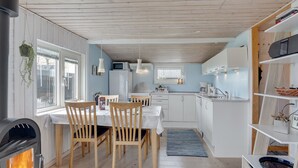 Een gezellige keuken met houten kastjes, een eettafel met stoelen, een inbouwoven en een klein raam.
