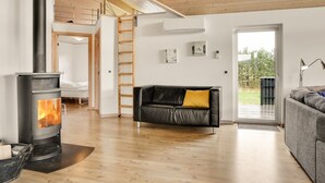 Ein modernes Wohnzimmer mit Kaminofen, einem schwarzen Ledersofa mit gelbem Kissen, einem grauen Sofa und einer Holzbalkendecke.