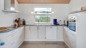 A modern kitchen with white cabinets, a stainless steel sink, a built-in oven, and a window with a view of greenery outside. - "Kimi" - 800m from the sea by Interhome (Glesborg)