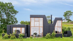 Una casa moderna de dos pisos con amplios ventanales y techo plano, rodeada por un campo cubierto de hierba y árboles.