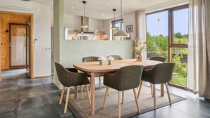 Een moderne eetruimte met een houten tafel en vier stoelen, een keuken achtergrond en een groot raam met uitzicht op groen.